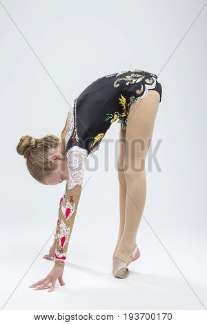 Sport Ideas. Young Caucasian Female Rhythmic Gymnast Athlete In Professional Competitive Suit Doing Backbend Stretching Exercise While Posing in Studio Against White. Vertical Image