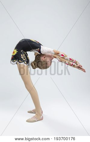 Sport Ideas. Young Caucasian Female Rhythmic Gymnast Athlete In Professional Competitive Suit Doing Backbend Stretching Exercise While Posing in Studio Against White. Vertical Image Composition
