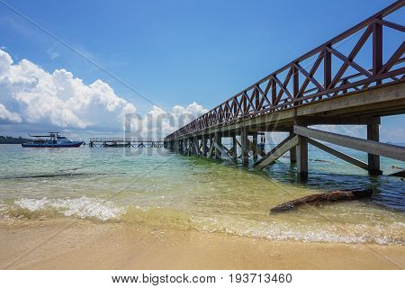 Wooden jetty over the beautiful Rusukan Besar island tropical beach with blue sky & clouds in Labuan,Malaysia.Labuan Island is also known as the Pearl of South China Sea.