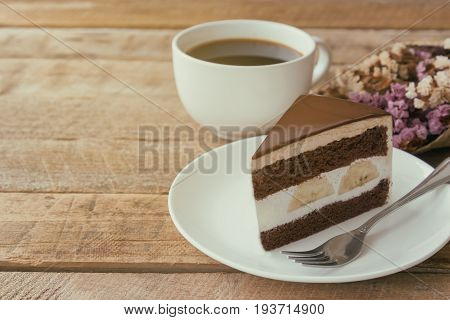 Banana chocolate cake on white plate served with black coffee. Chocolate cake layered with whipped cream and banana look so delicious. Enjoy eating at cafe restaurant with chocolate cake and coffee.