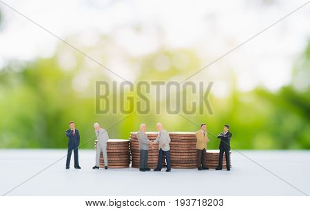 Stack of coins behind miniature businessman handshaking ,discussing and negotiating using as commitment ,agreement ,investment and partnership background concept.