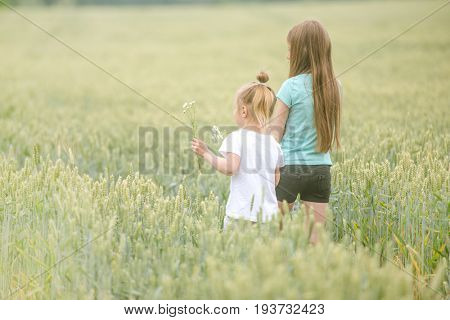 sisters walking through field, picking flowers, backshot