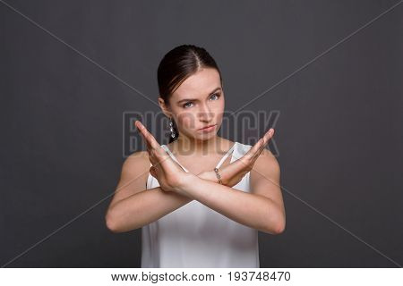Woman making stop sign with crossed hands. Serious girl denying, refusing any action, looking at camera, dark background