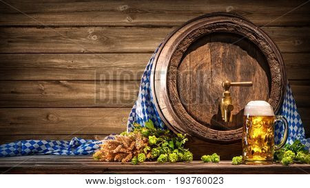 Oktoberfest beer barrel and beer glass with wheat and hops on wooden table