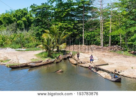 Ivoloina Madagascar - December 22 2015: Malagasy countryside people from the village unload sand from traditional handmade dugout wooden boats near the city of Toamasina (Tamatave) Madagascar East Africa. Everyday life on the river.