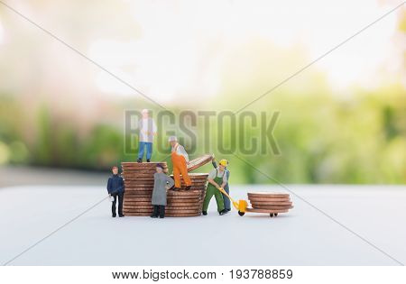 Miniature businessman and worker standing on the coins and carrying coins using as a business concept.