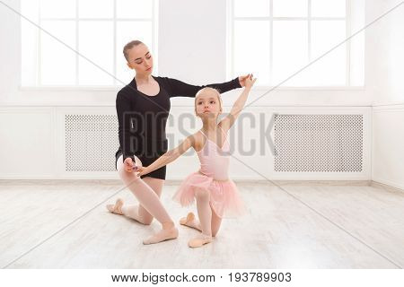 Little girl learning ballet with teacher copy space. Cute small ballerina training classical dance exercises with female coach.