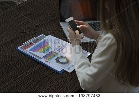 Asian smile beautiful girl sitting outdoor office using smart phone and laptop in nature. Work space with work sheet of business business and lifestyle conceptcopy space