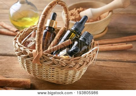 Bottles of cinnamon oil in basket on wooden background