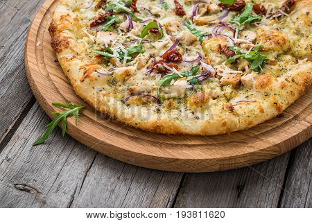 pizza with sun-dried tomatoes, prosciutto, arugula and parmesan cheese on a plate on the table