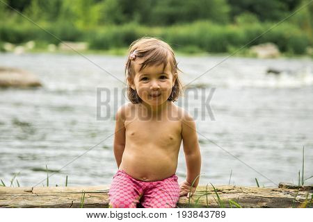 Little Girl Sitting On A Log Near The River