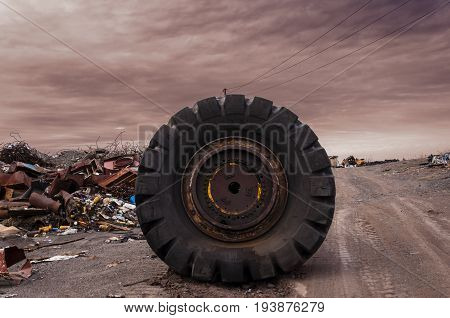 huge wheel from a truck on a dirt road in the middle of a garbage dump part of a rear axle