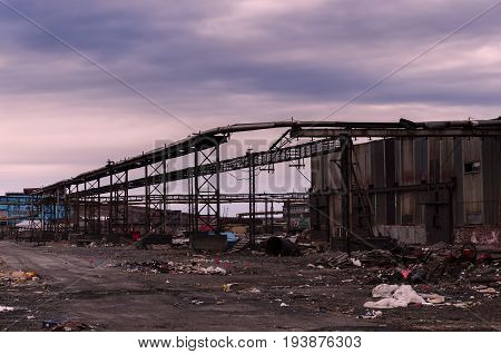 Old abandoned back in the middle of a huge garbage dump of various metal scraps and boards against the background of a stormy sky