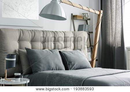 Grey bed with quilted headboard and big wooden lamp