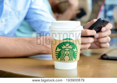Bangkok Thailand - May 20 2015 : Starbucks paper coffee cup on the table with a man using smartphone as background in Starbucks coffee shop.