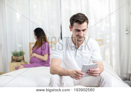 Man Using Tablet With Ignor Pregnancy Woman At Bedroom Family Concept.