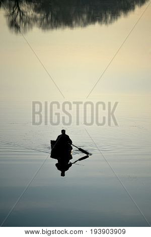 mirror surface of the river, a fisherman sitting in the boat and go fishing in the morning