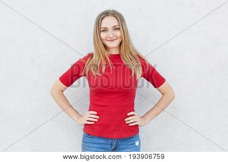Glad Female With Light Hair And Blue Eyes Having Smile On Her Face Wearing Red Sweater And Jeans Hol