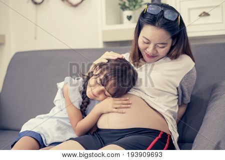 Closeup Of Happy Child Listen To Belly Of Pregnant Woman. Family Having Fun Indoor. Mothers Day Conc