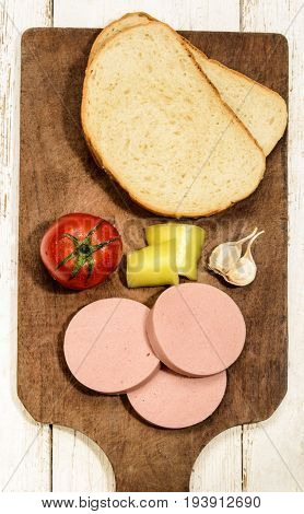 raw scalded sausage with tomato yellow pepper garlic and bread on a wooden board