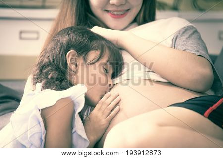 Closeup Of Happy Child Kiss To Belly Of Pregnant Woman. Family Having Fun Indoor. Mothers Day Concep