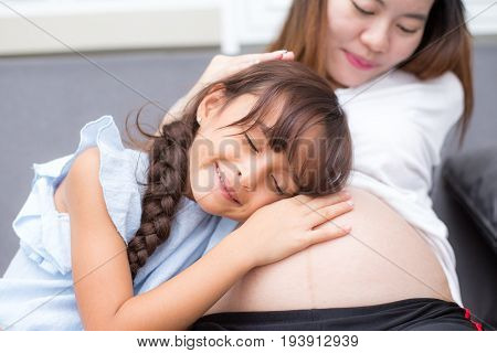 Closeup Of Happy Child Listen To Belly Of Pregnant Woman. Family Having Fun Indoor. Mothers Day Conc