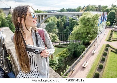 Young female traveler with photocamera enjoying beautiful cityscape view on the green valley with bridge and garden in Luxembourg city