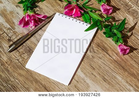 Mocap. Notepad with white paper and pen, decorated with a sprig of pink flowers on a plastic surface, simulated wood,