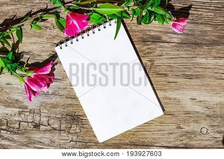 Mocap. Notepad with white paper decorated with a sprig of pink flowers on a plastic surface, simulated wood, top view