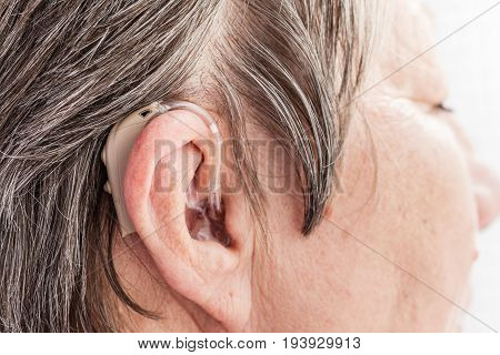 Closeup senior woman with hearing aid in her ear. Health care hear amplify device for the deaf.