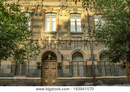 Facade of old building of multi-colored tufa stone with carved archescolumns and cornices surrounded by trees