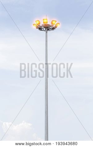 Sportlights tower illuminated in stadium with cloudy blue sky in background.