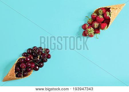 Berries in waffle cones - strawberry and black cherry on blue background. Top view. Copy space. Still life mockup flat lay