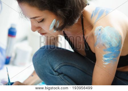Woman sits in pofile and works on watercolor painting. Art therapy painting concept. girl with paintbrush gets messed in paints