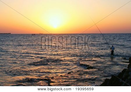 Рыбак и на море в вечернее время на закате