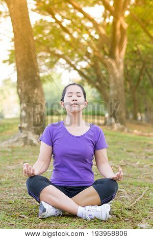 Asian woman maditationing alone on yard in the park with yellow light of sun light