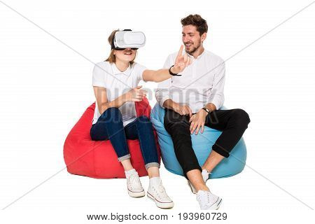 Smiling friends experiencing virtual reality glasses seated on beanbags isolated on white background. Experiencing virtual gaming adventure. VR