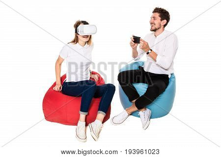 Smiling friends experiencing virtual reality glasses seated on beanbags isolated on white background. Experiencing virtual gaming adventure. VR