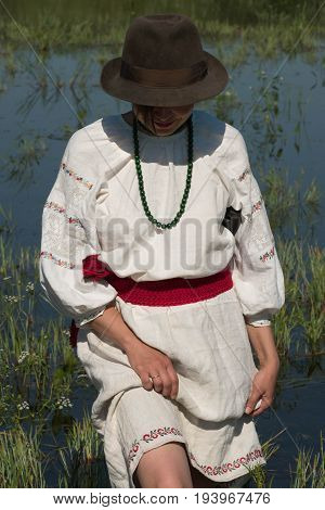National clothes - a girl standing in a pond in a hat with a machete