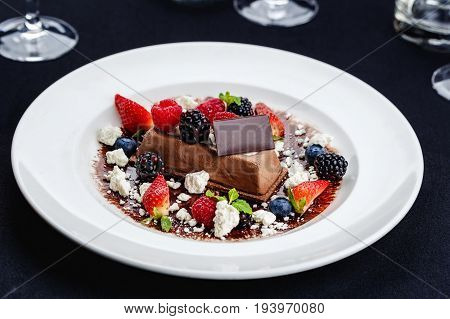 A chocolate bar served on a white plate decorated with berries and pieces of biz.