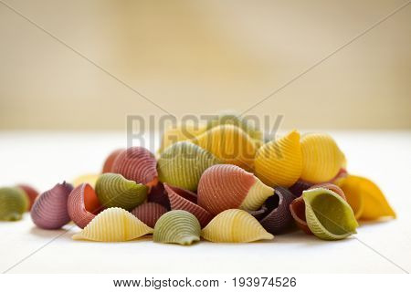 a pile of uncooked conchiglie, italian seashell pasta, with different colors: yellow as usual, red made with tomato and green made with spinach