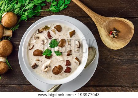 An overhead photo of a plate of a mushroom cream soup with champignons, cremini, fresh parsley, and peppercorns, on a dark rustic background texture with a place for text