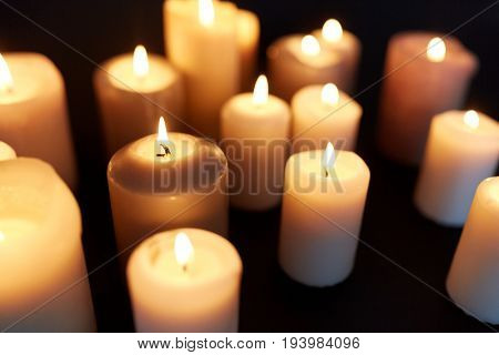 mourning and commemoration concept - candles burning in darkness over black background