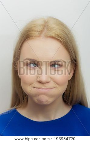 Woman squinting eyes and puffing cheeks on funny face. Cute girl with crossed grey eyes healthy skin and long blond hair in blue dress on white background. Grimace and facial expression. Strabismus