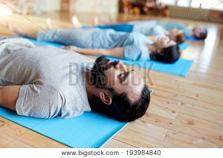 fitness, sport and healthy lifestyle concept - group of people doing yoga corpse pose on mats at studio