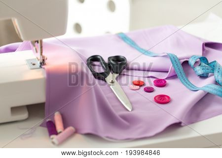 needlework, technology and tailoring concept - sewing machine with scissors, buttons, tape measure and fabric