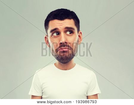emotion, facial expressions and people concept - sad young man in white t-shirt over gray background looking up (funny cartoon style character with big head)