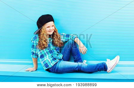 Street fashion concept - stylish kid little girl with curly hair on a blue background