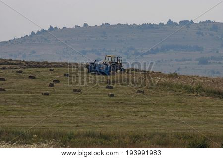 Harvesting hay tractor work on field make haystacks, Plana mountain, Bulgaria