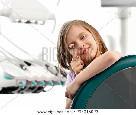 Kid Girl In A Big Dental Chair Plays With Dental Mirror On Background With Stomatologist Office Eqiu